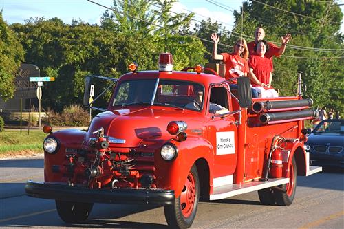 old fashioned fire truck with mayor, city council members riding on top